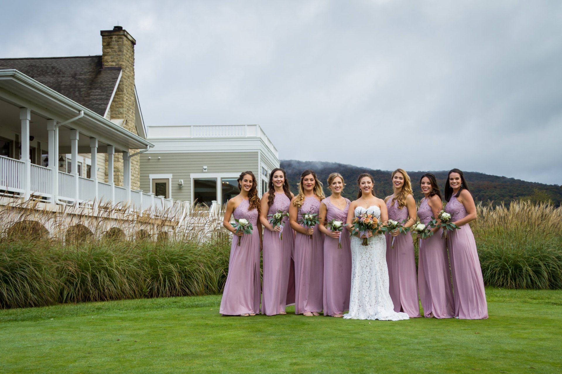 A group portrait of the bride and bridesmaids on a green lawn with mountains and the venue in the background