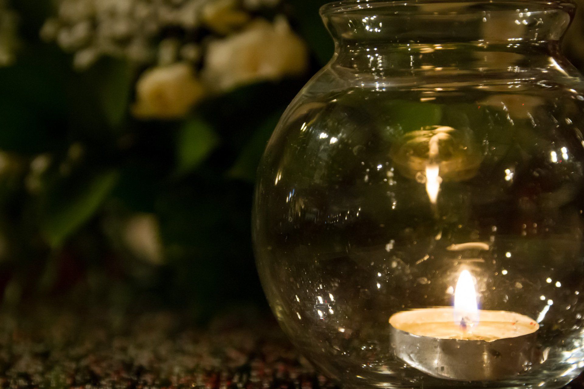 A close up view of a table centerpiece showing flowers and a candle in a clear glass globe