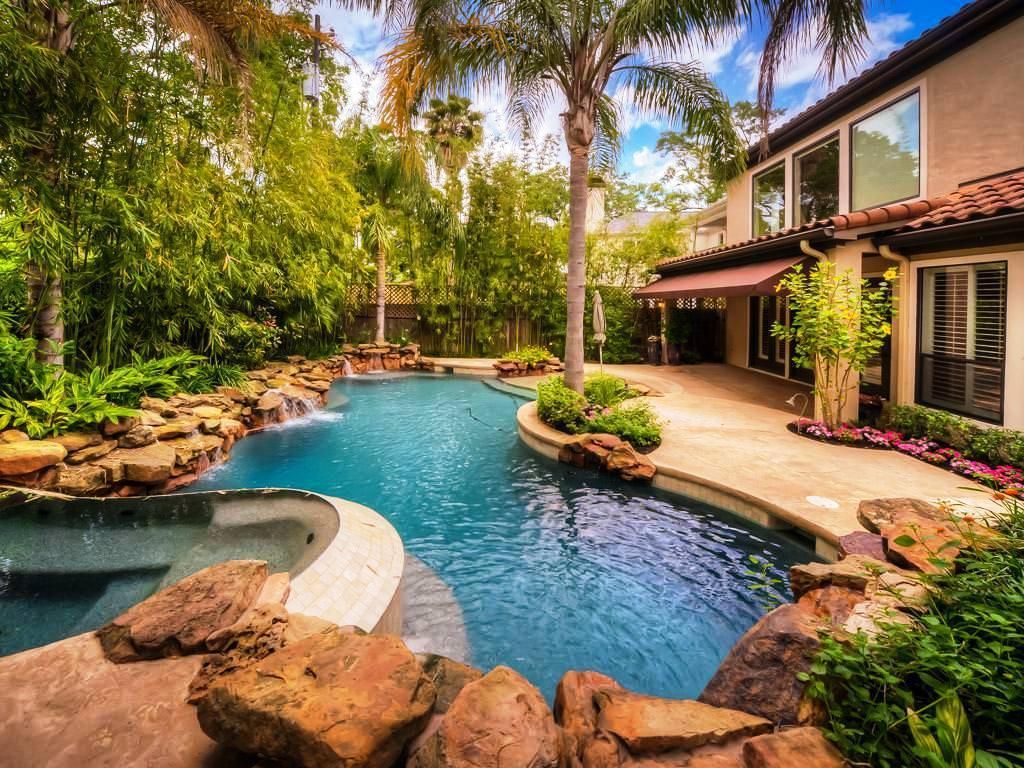 A residential pool surrounded rocks and a fence lined with thick trees and shrubs