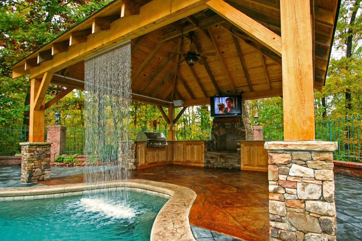 A stone and wood canopy with a waterfall pouring down the roof into a pool