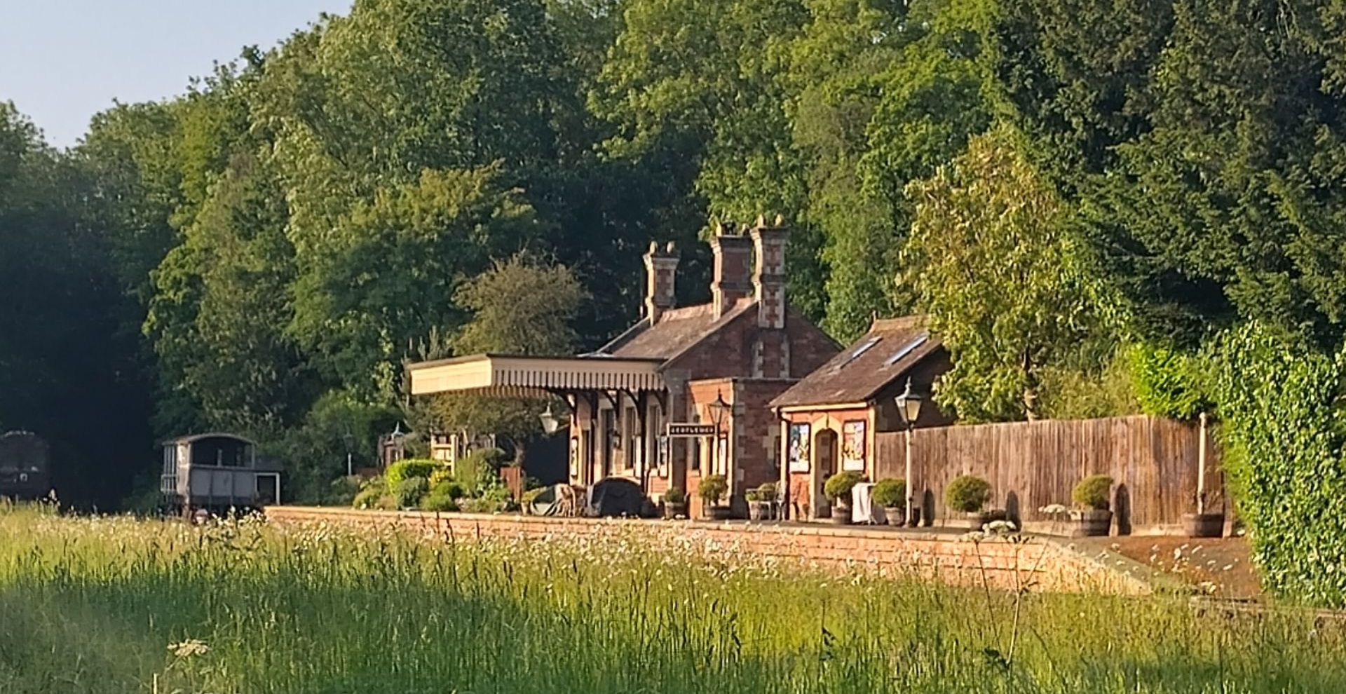 A railtrack view of the station buildings on platform 1 on the right, a blue sky and the railwacy carriage in the background housed on the green platform 2.
