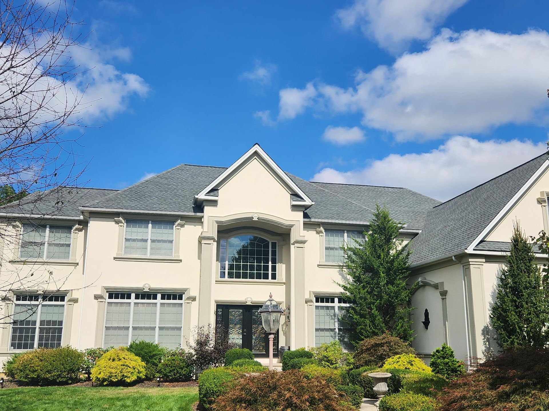 Front view of a large, elegant suburban home with manicured landscaping and a bright blue sky overhe