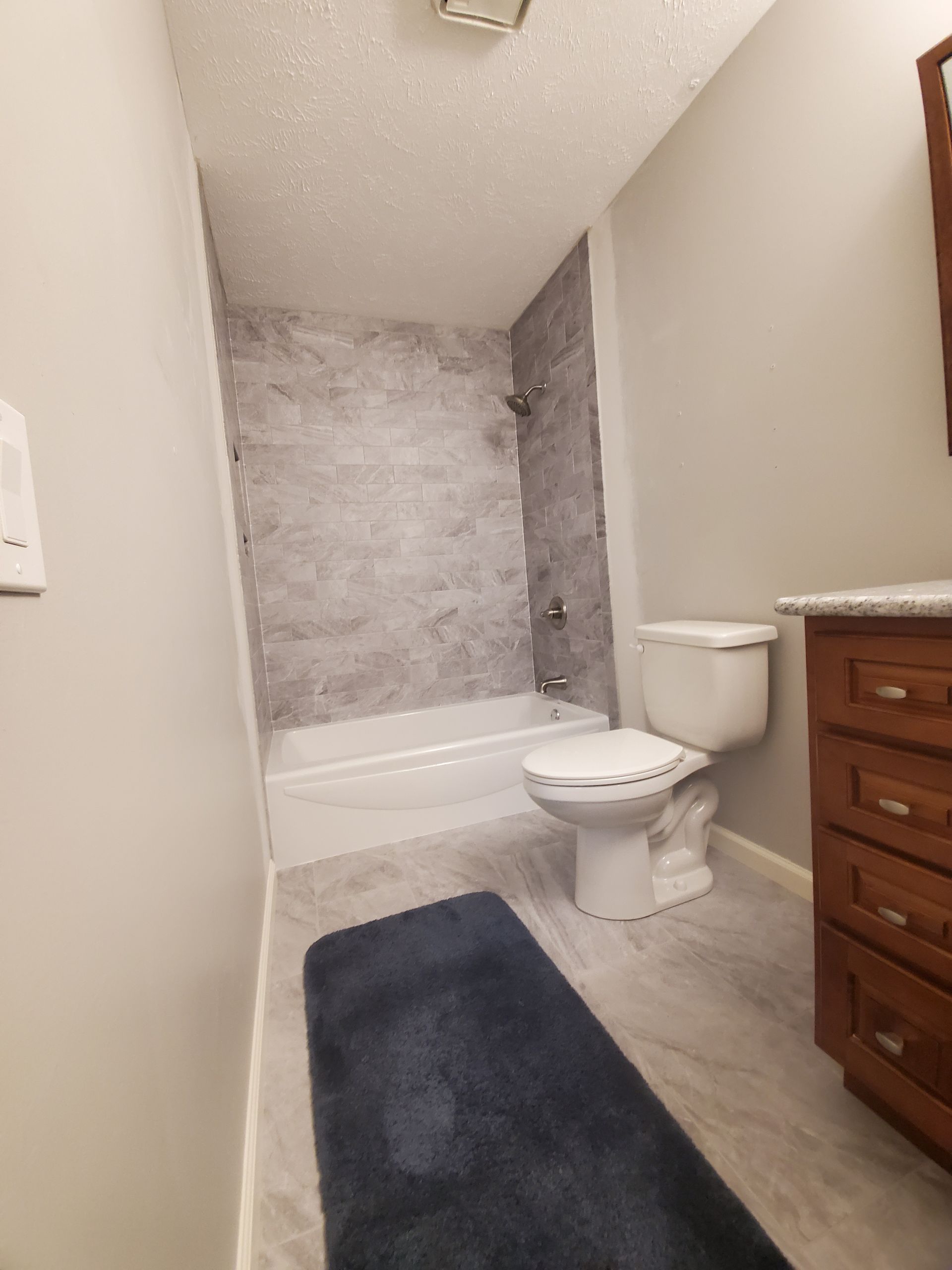 Simple and stylish bathroom remodel on a budget Affordable bathroom remodel with gray tile, white bathtub, and modern flooring