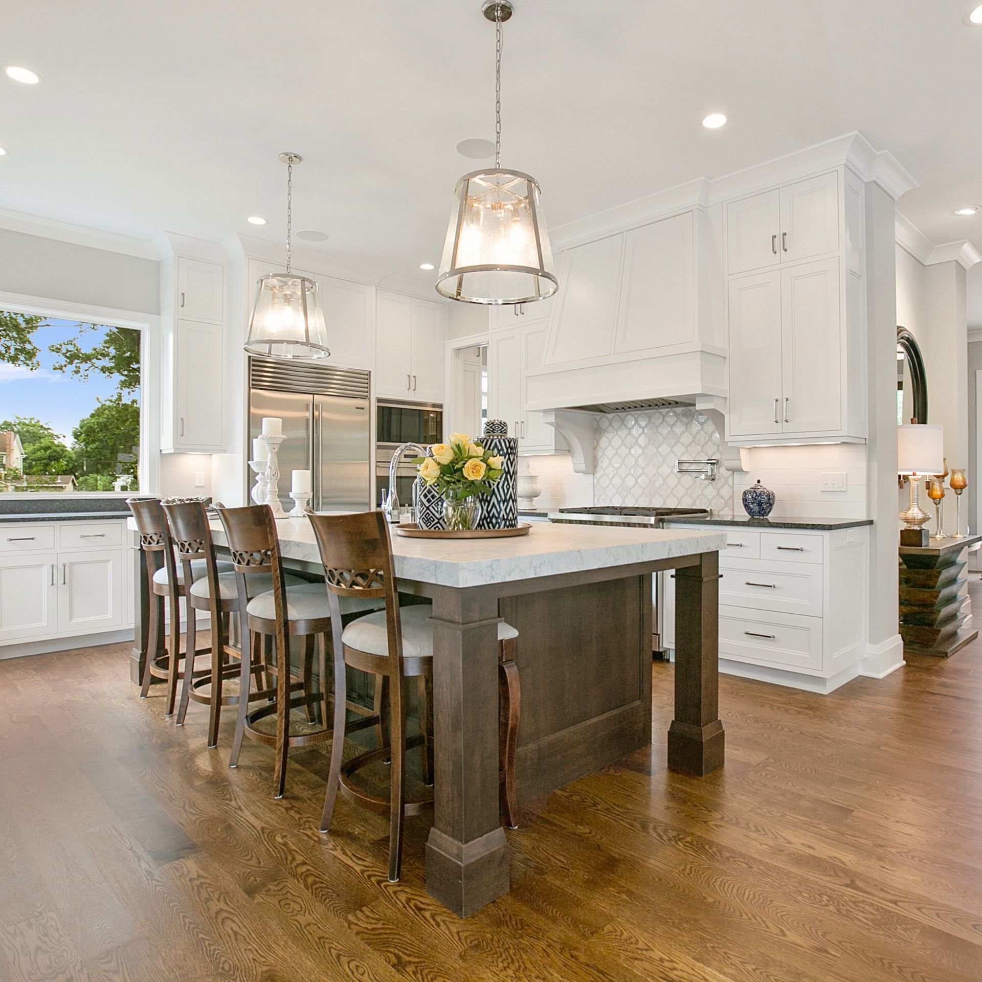 Bright, elegant kitchen with white shaker cabinets, a large dark wood island, pendant lighting, and