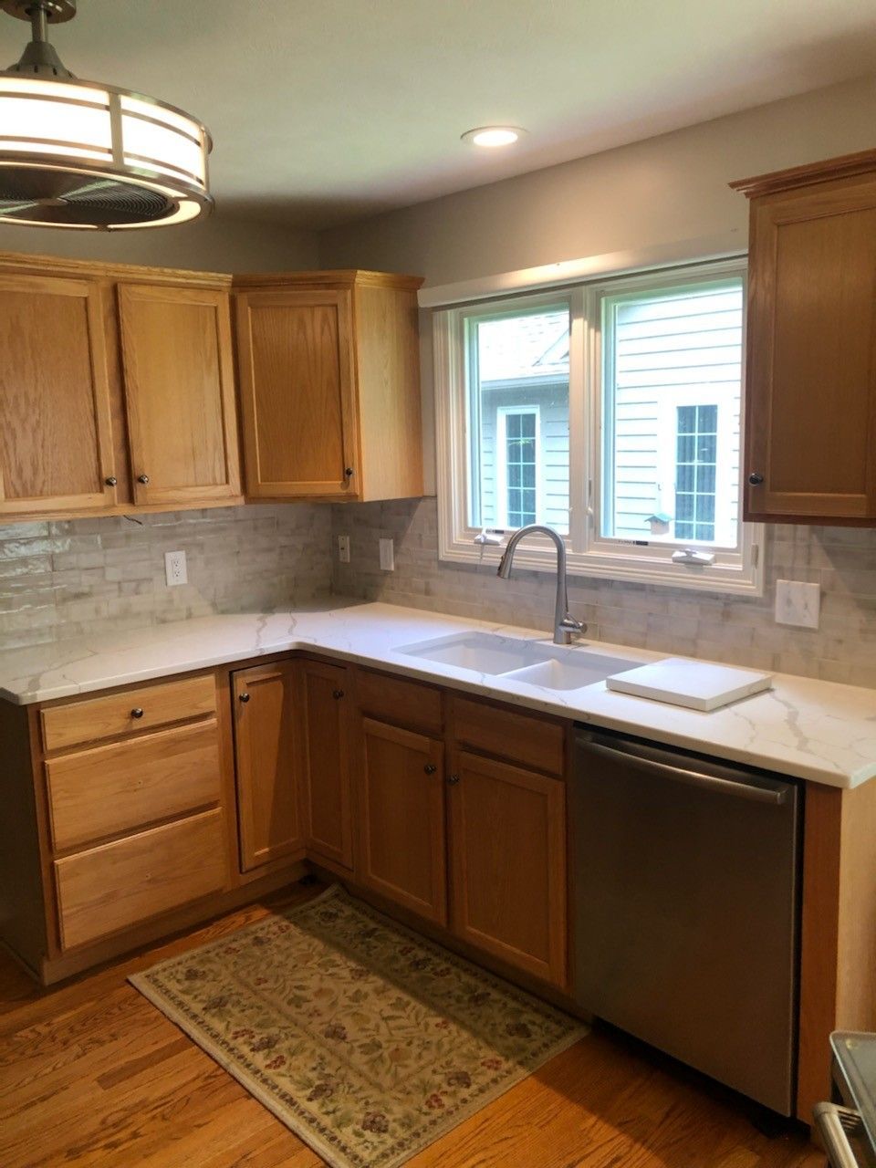 Remodeled kitchen with oak cabinets, modern backsplash, and stainless steel sink under window