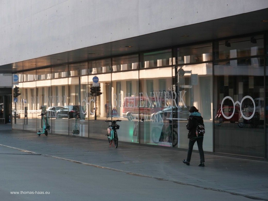Passantin, gespiegelter Straßenverkehr und ruhende Verkehrsmittel... Bewegung: Passantin, gespiegelter Straßenverkehr und ruhende Verkehrsmittel...