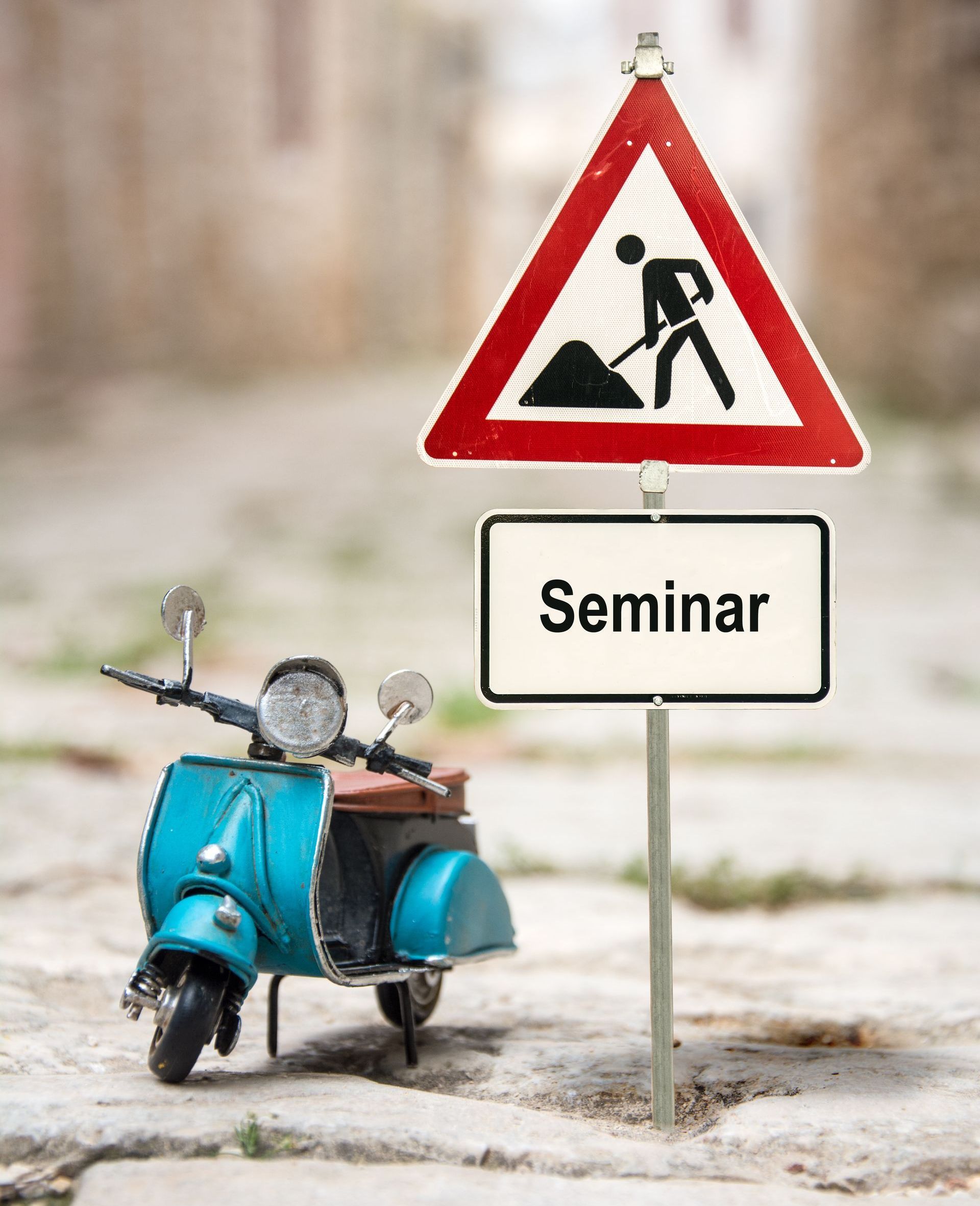 Ein blauer Roller, daneben ein Baustellenschild mit dem Untertitel „Seminar“ Ein blauer Roller, daneben ein Baustellenschild mit dem Untertitel „Seminar“