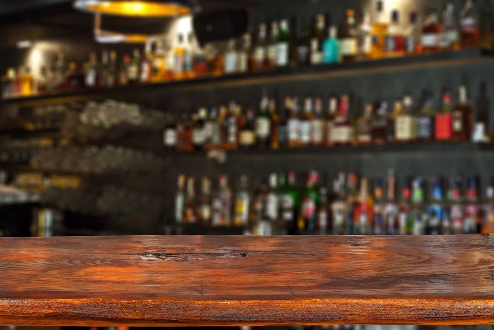 A wooden bar table with a bottle of liquor positioned in the background, creating a cozy atmosphere.