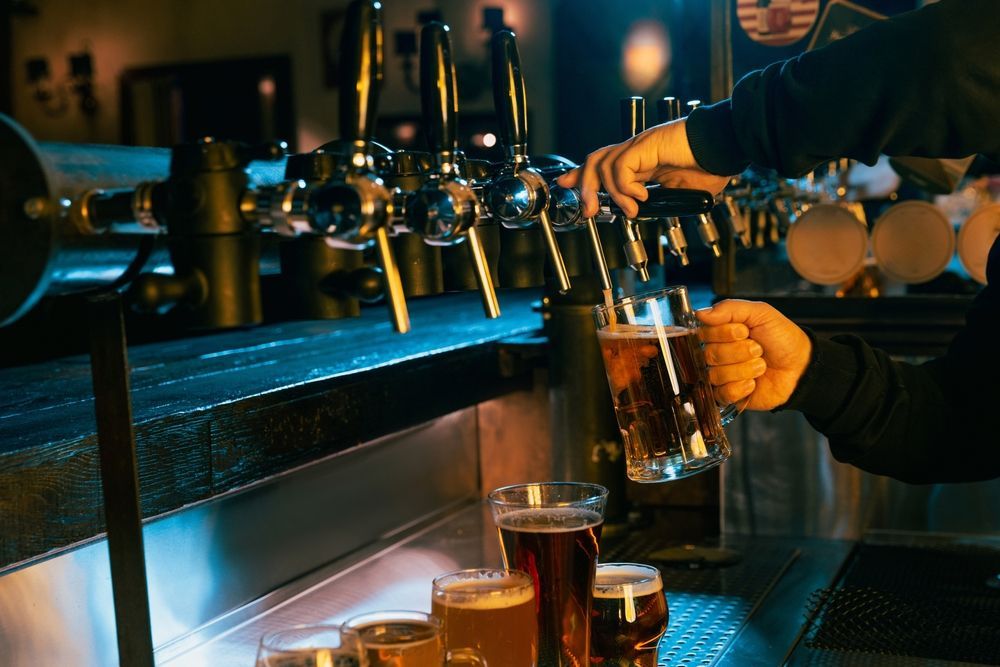 A man is pouring a golden beer from a bottle into a clear glass, creating a frothy head.