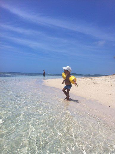 Moment de douceur sur l’îlet Long : un bébé marche sur la plage, avec la mer en toile de fond.
