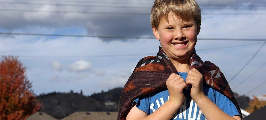 A smiling boy with a blanket as a cape.