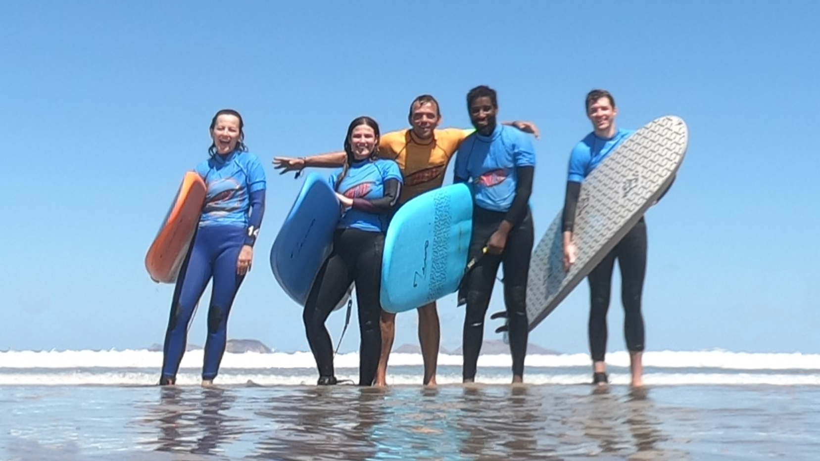 4 surfers entering the water as the sun rises over the cliffs of famara