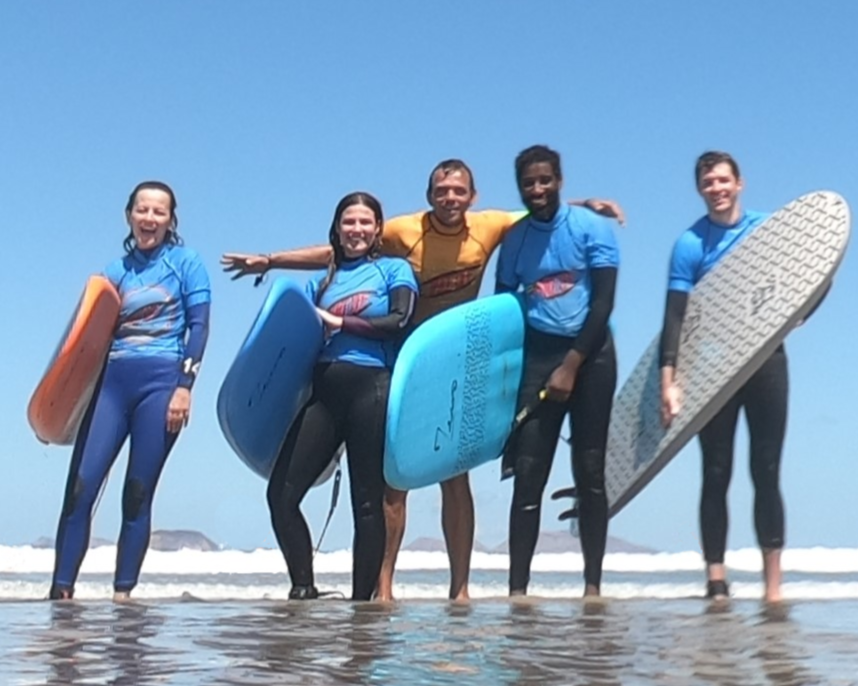 4 surfers entering the water as the sun rises over the cliffs of famara
