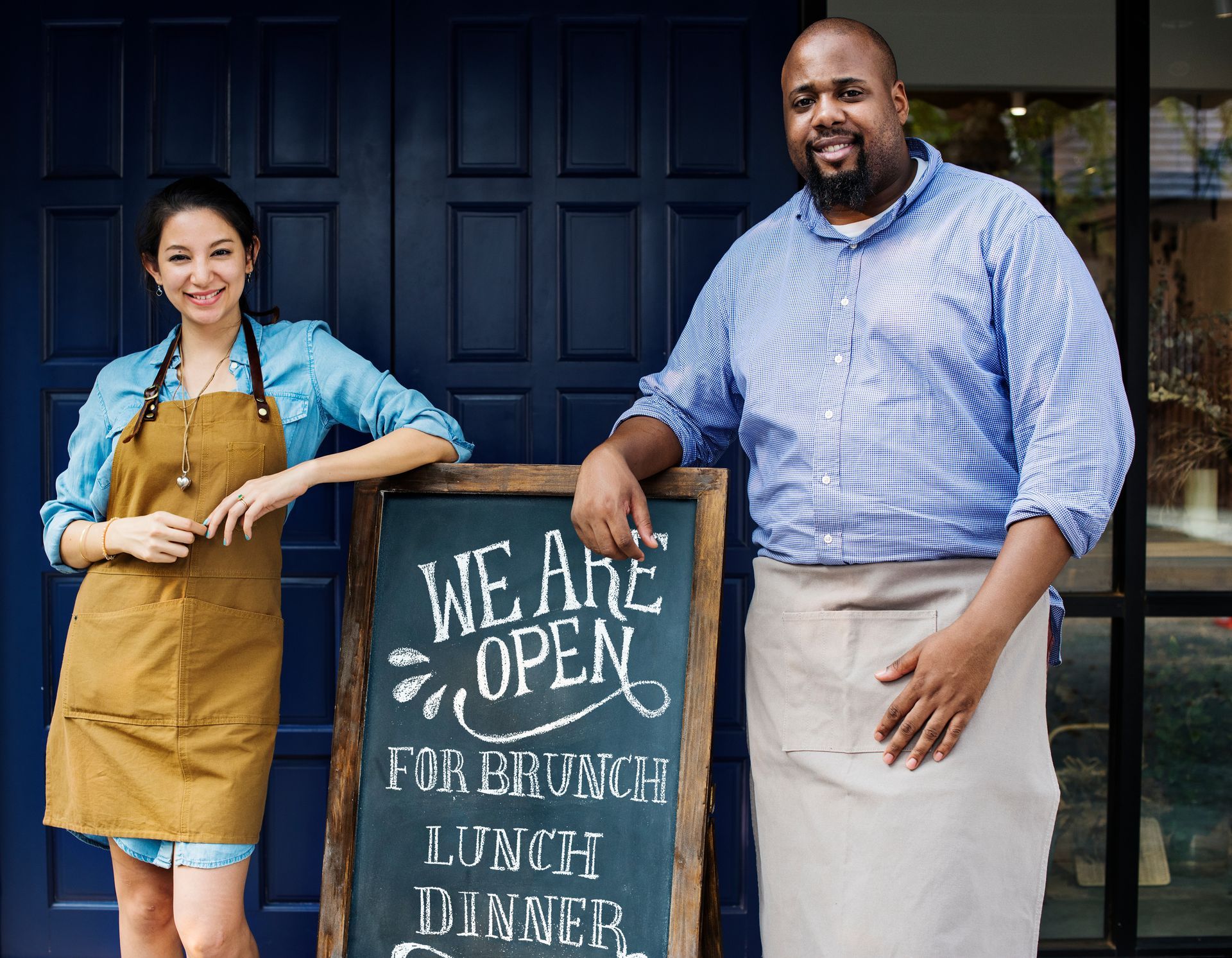 front of restaurant, man and woman, board with open for brunch, lunch, and dinner message