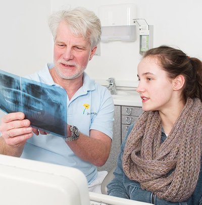 Zahnarzt Dr. Christian Köhne zeigt einer jugendlichen Patientin in einem Rötgenbild, wo die Ursache für Ihr Zahnproblen liegt