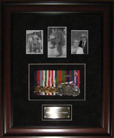 Photos, medal rack, and engraved brass plate framed in a mahogany shadow box with black suede mats
