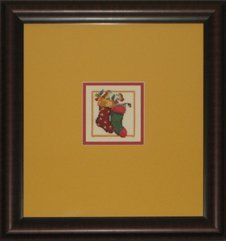 Small cross-stitch of 2 Christmas stockings framed in a brown frame with golden yellow and red mats