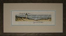 Cross-stitch of a lighthouse in a storm framed in a brown rustic frame with taupe and grey mats