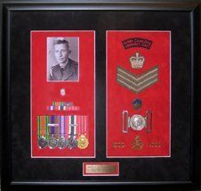Portrait photo, medal rack and ribbon bar, RCOC cap badges, shoulder patches, belt buckle framed in a black shadow box with black and red suede mats