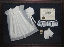 Christening gown and baby items shadow box Christening gown, birth certificate, baby photos framed in a mahogany shadow box with blue suede mats