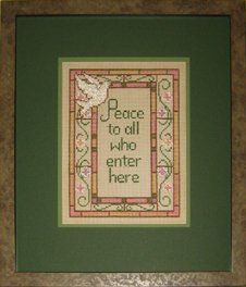 Cross-stitch of a stained glass window with a peace verse framed in a taupe burl frame with dark and light green mats