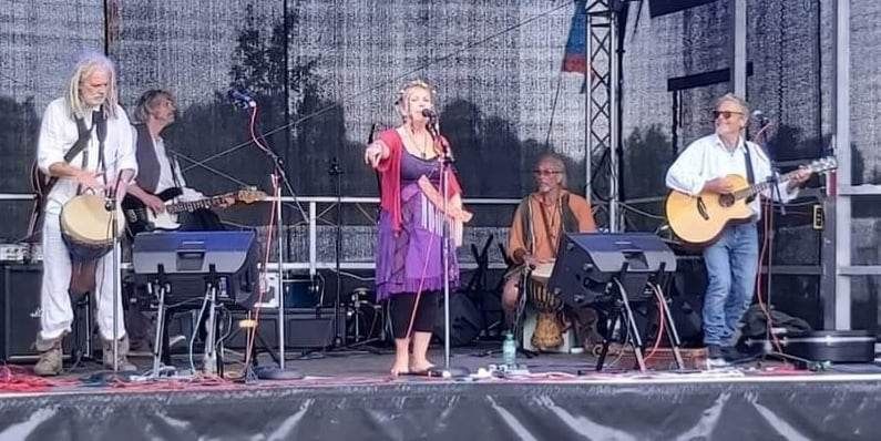 Kindred spirit, a Five piece prog rock folk band with fleetwood mac undertones play their instruments under ethereal blue lights to a crowd. The memebrs are happy and consuemd by their music. #pagan music #paganfestival #greenoaksgathering