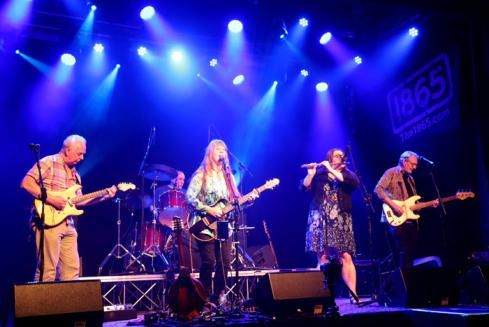 Kindred spirit, a Five piece prog rock folk band with fleetwood mac undertones play their instruments under ethereal blue lights to a crowd. The memebrs are happy and consuemd by their music. #pagan music #paganfestival #greenoaksgathering