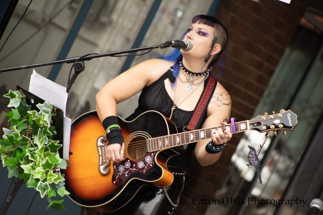 'Shelly the Alternative folkie' is a young woman playing acustic guitar singing folk song with bright coloured hair and a microphone. #paganmusic #folkmusic #alternative #indie