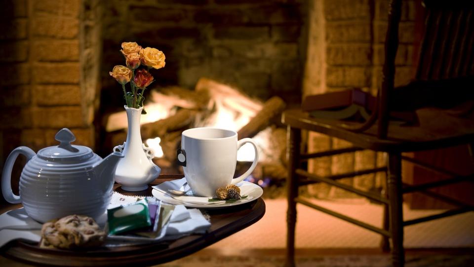 Ein Teeservice steht im Vordergrund eines gemütlichen Kaminfeuers