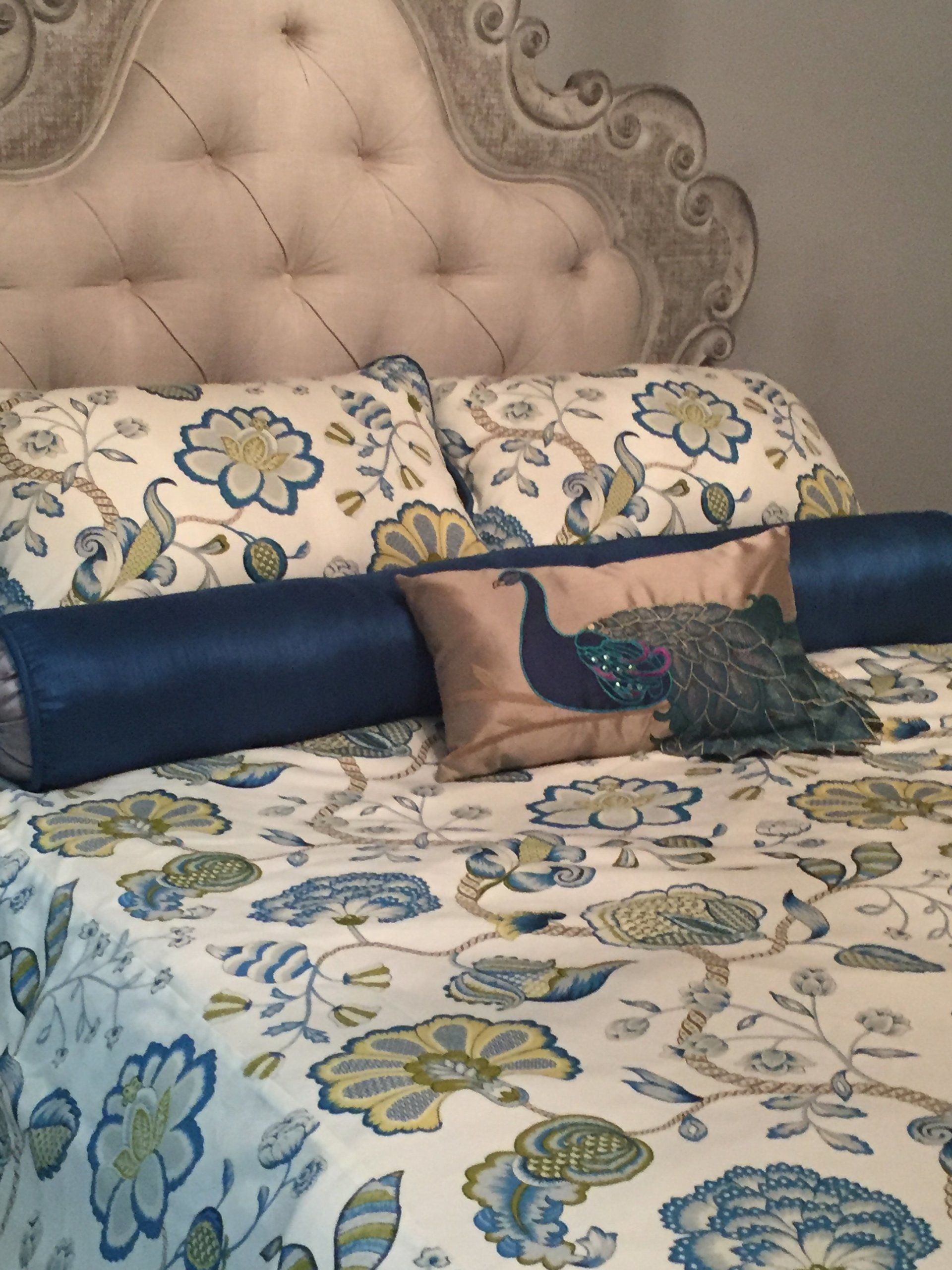 Example of duvet cover in gold, teal and green with large round teal pillow and matching pillow with peacock embroidery.