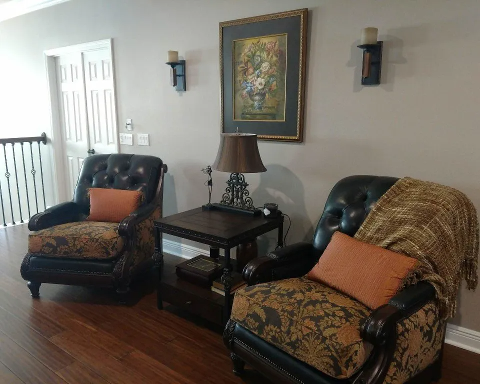 Large occasional library chairs in black kid leather and black and gold tones sides and cushions with silk pillow, side table with aluminum legs, coordinating art on wall with sconces.