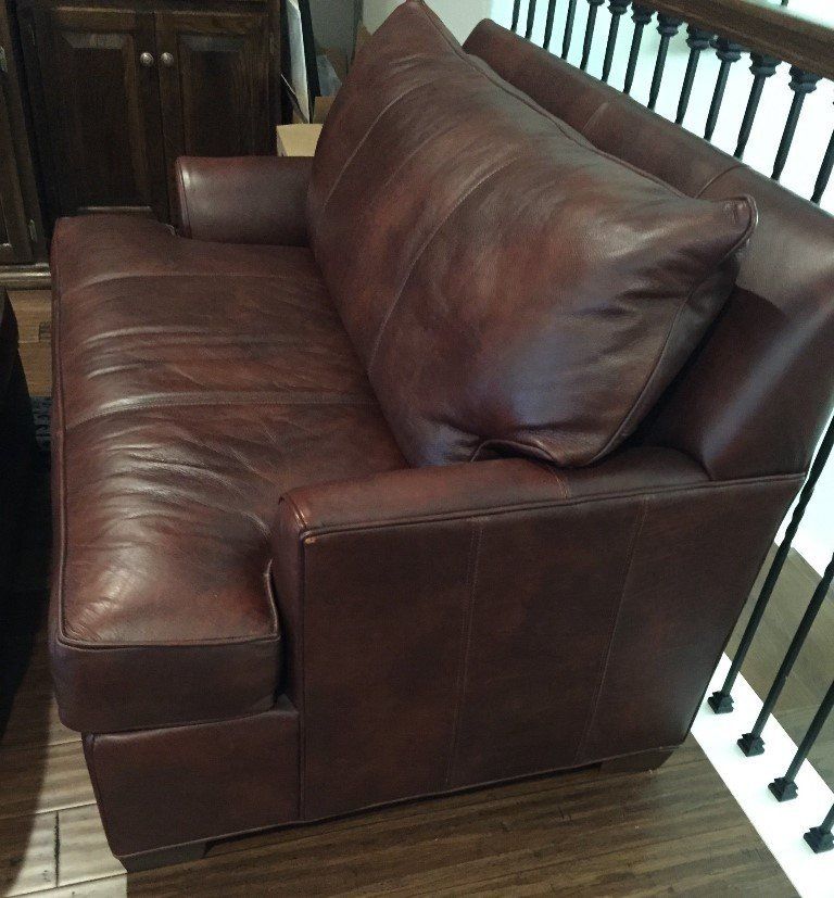 Brown leather love seat with pillow back.