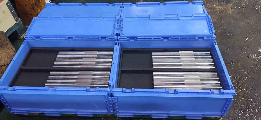 Ejes metálicos mecanizados en CNC organizados en contenedores industriales para producción en serie de componentes de precisión.