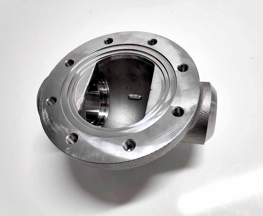Cuerpo de bomba mecanizado en CNC con brida y salida lateral, componente industrial de alta precisión para sistemas de fluidos.