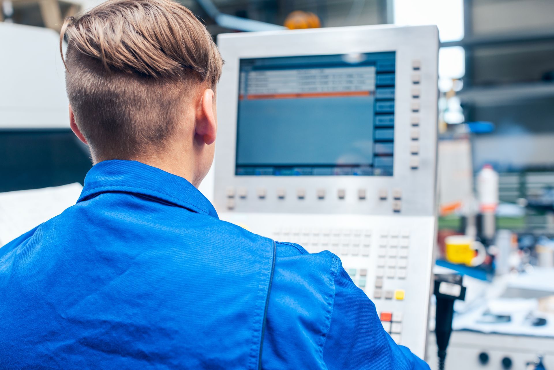 Operador de mecanizado CNC supervisando el control numérico de una máquina industrial durante el proceso de fabricación.