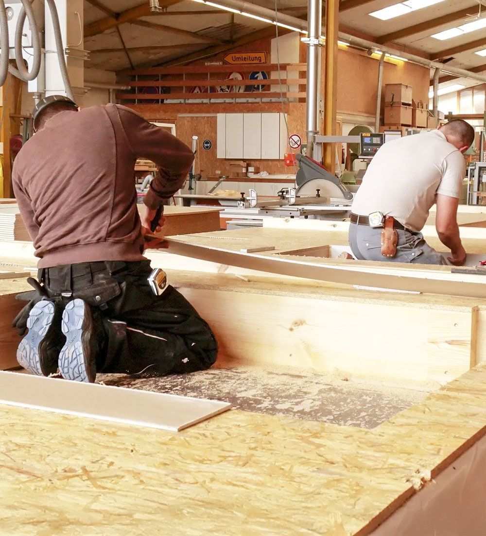 Zwei Arbeiter von Grübbel arbeiten einer Holzkonstruktion in einer Werkstatt