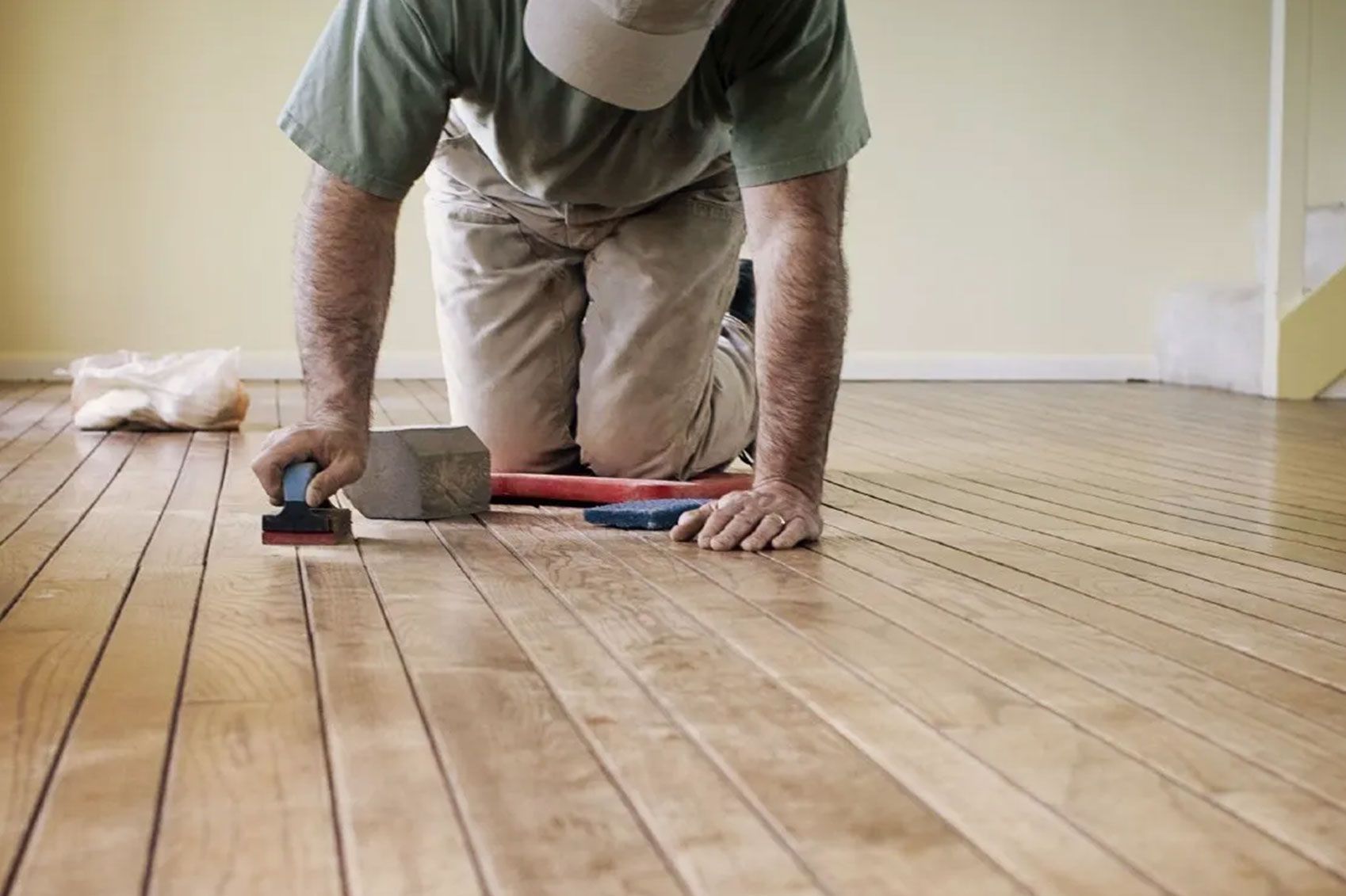 Ein Arbeiter auf Knien schmirgelt einen Holzboden ab