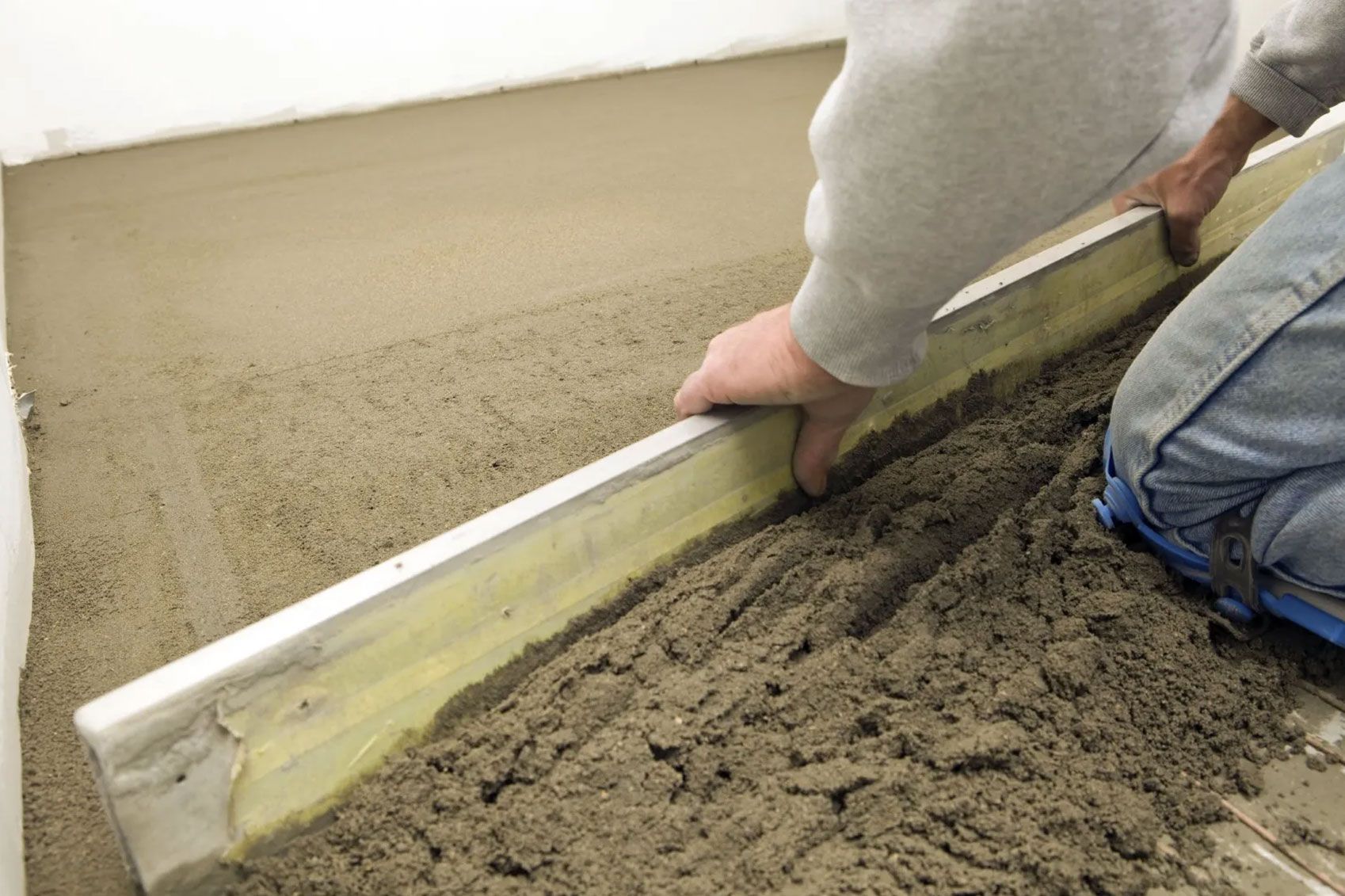 Ein Arbeiter auf Knien mit einem Holzbrett auf Sand