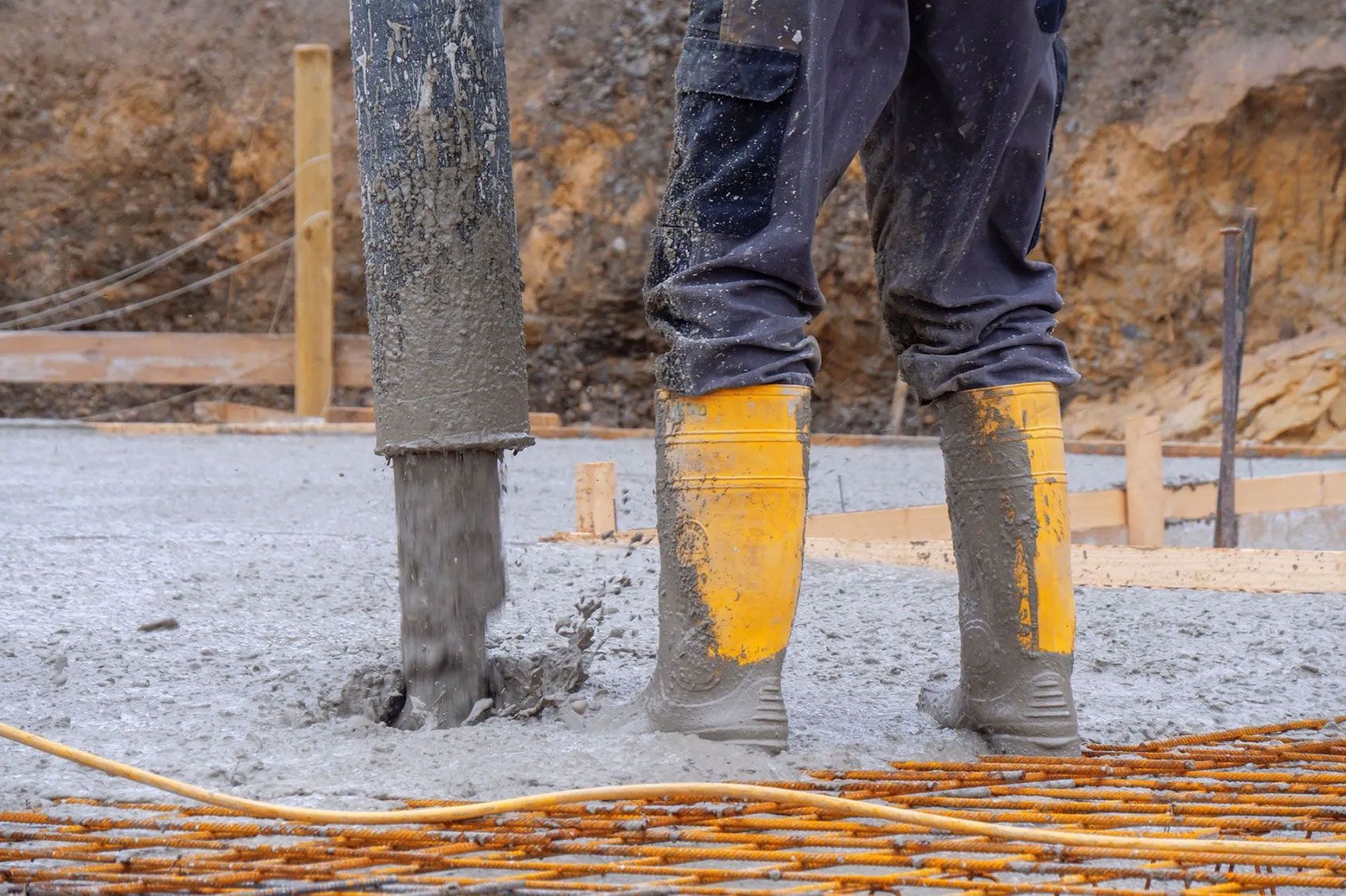 Ein Arbeiter mit gelben Gummistiefeln steht im Beton und arbeitet
