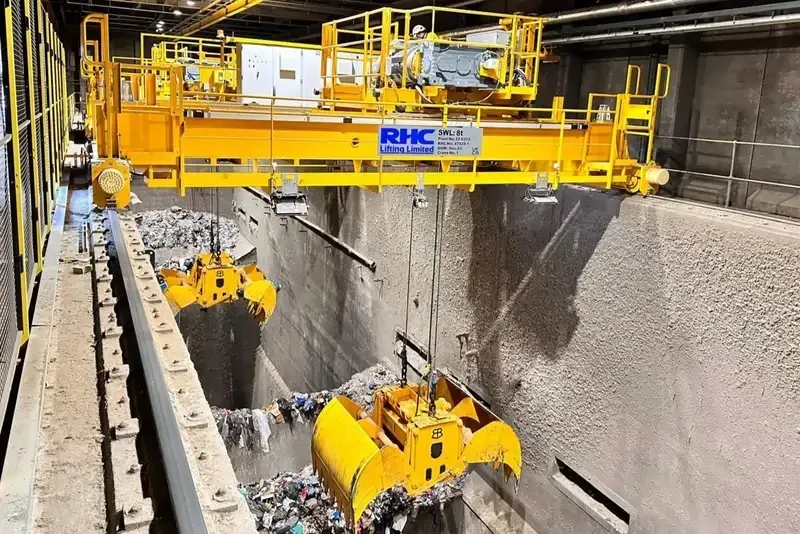 A yellow handling grab crane, positioned above a waste bunker