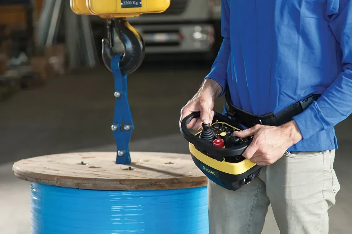 A man using an AUTEC radio remote to lift a large drum