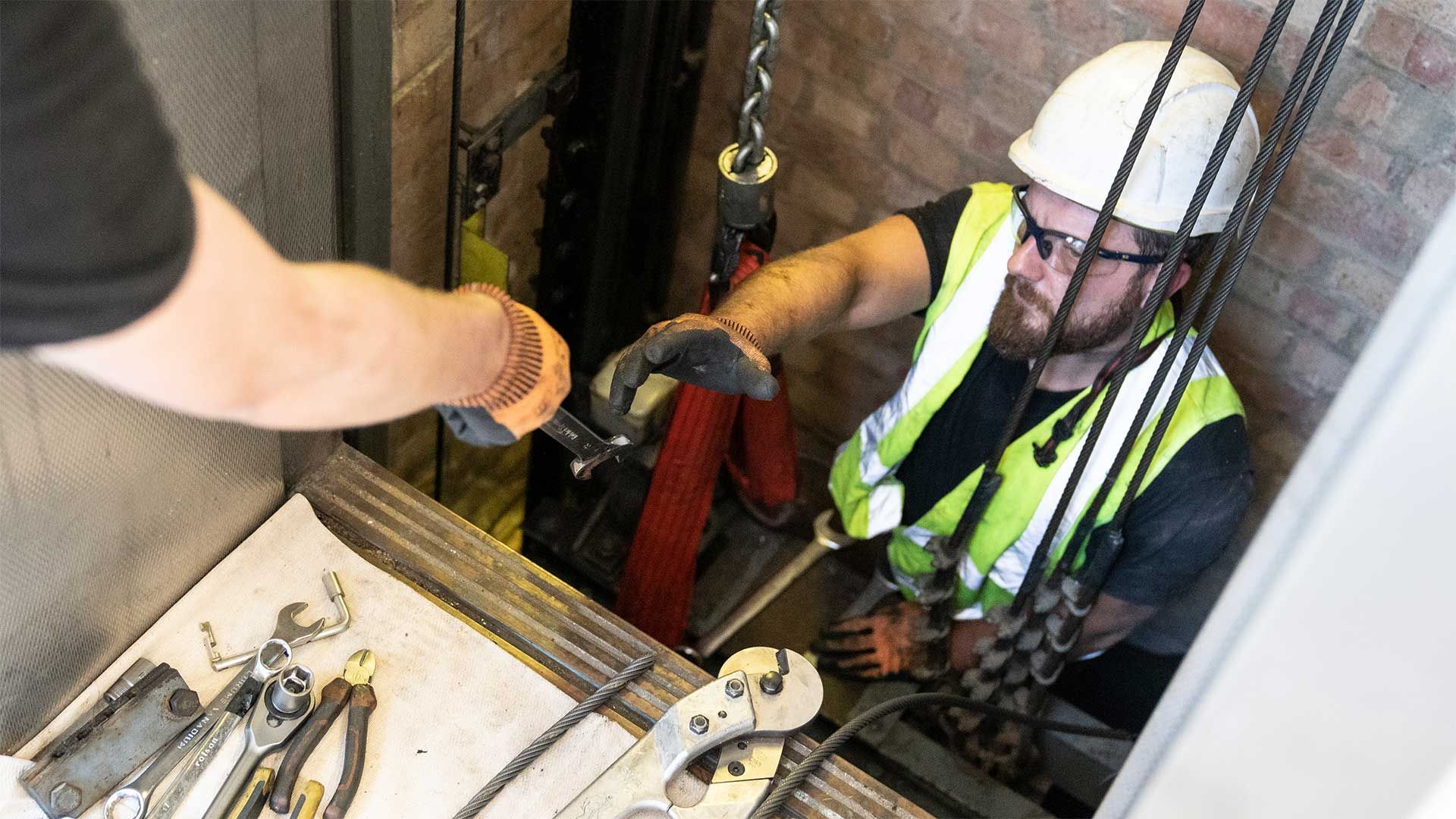 Engineer working in lift whilst tools are passed down to him