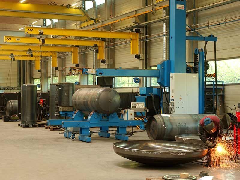 Multiple jib cranes in a workshop in the background, and an engineer welding in the foreground