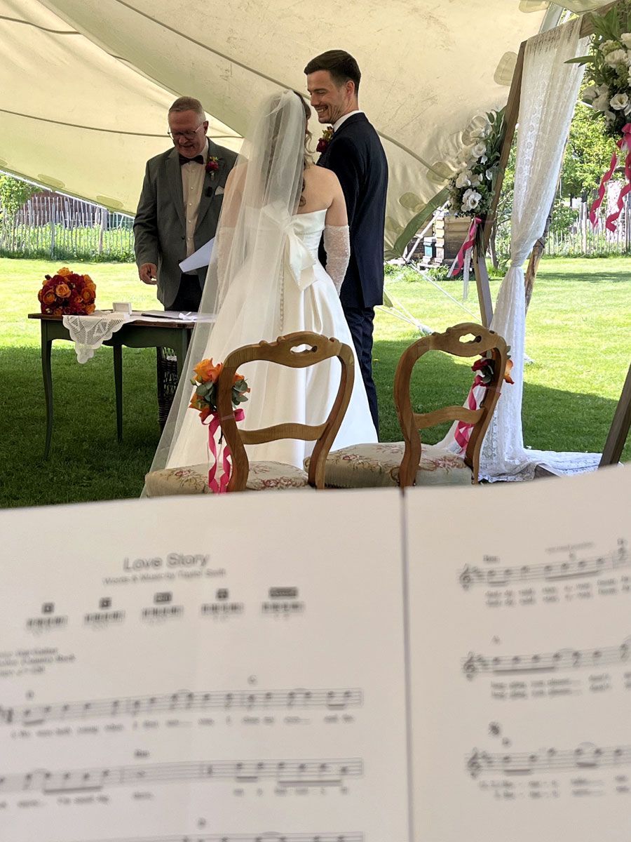 Hochzeitspianistin begleitet eine freie Trauung live am Piano an einem sonnigen Tag im Garten einer schönen Location.