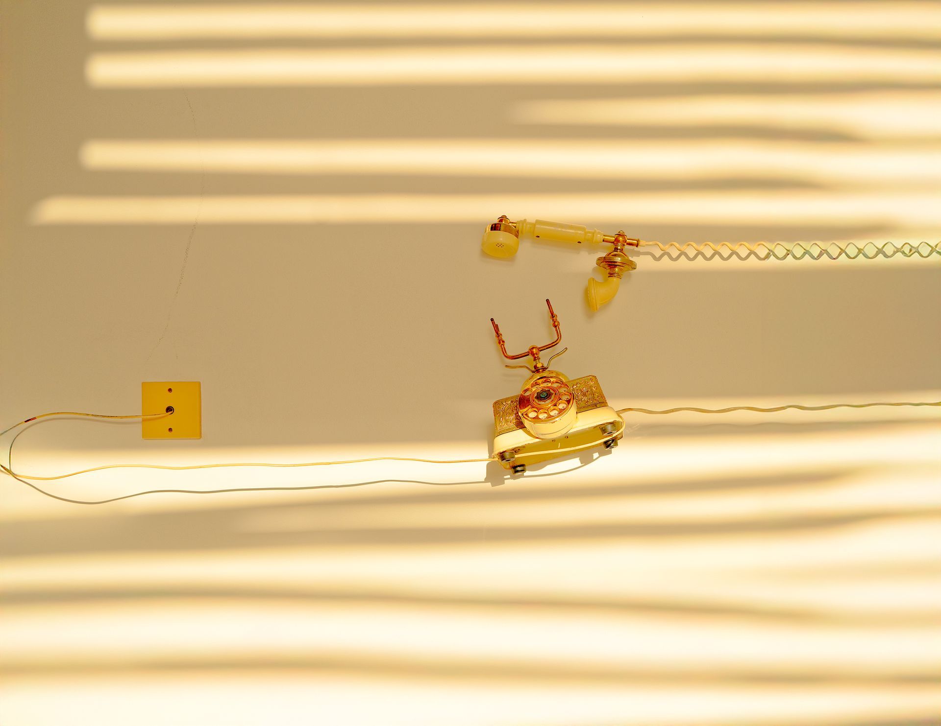 Disassembled old telephone on a bright wall, illuminated by warm yellow light and striped shadows.