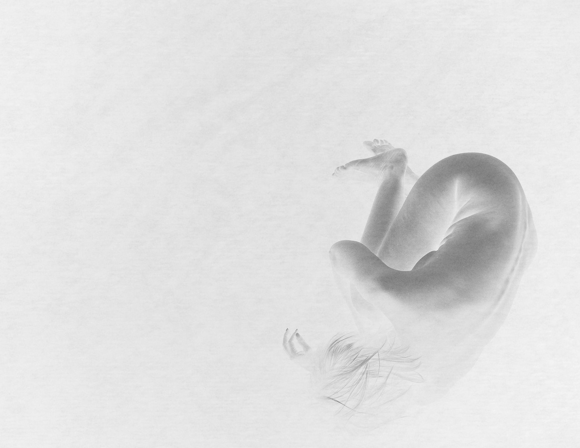 Black-and-white self-portrait of a woman curled in a fetal position on the floor.