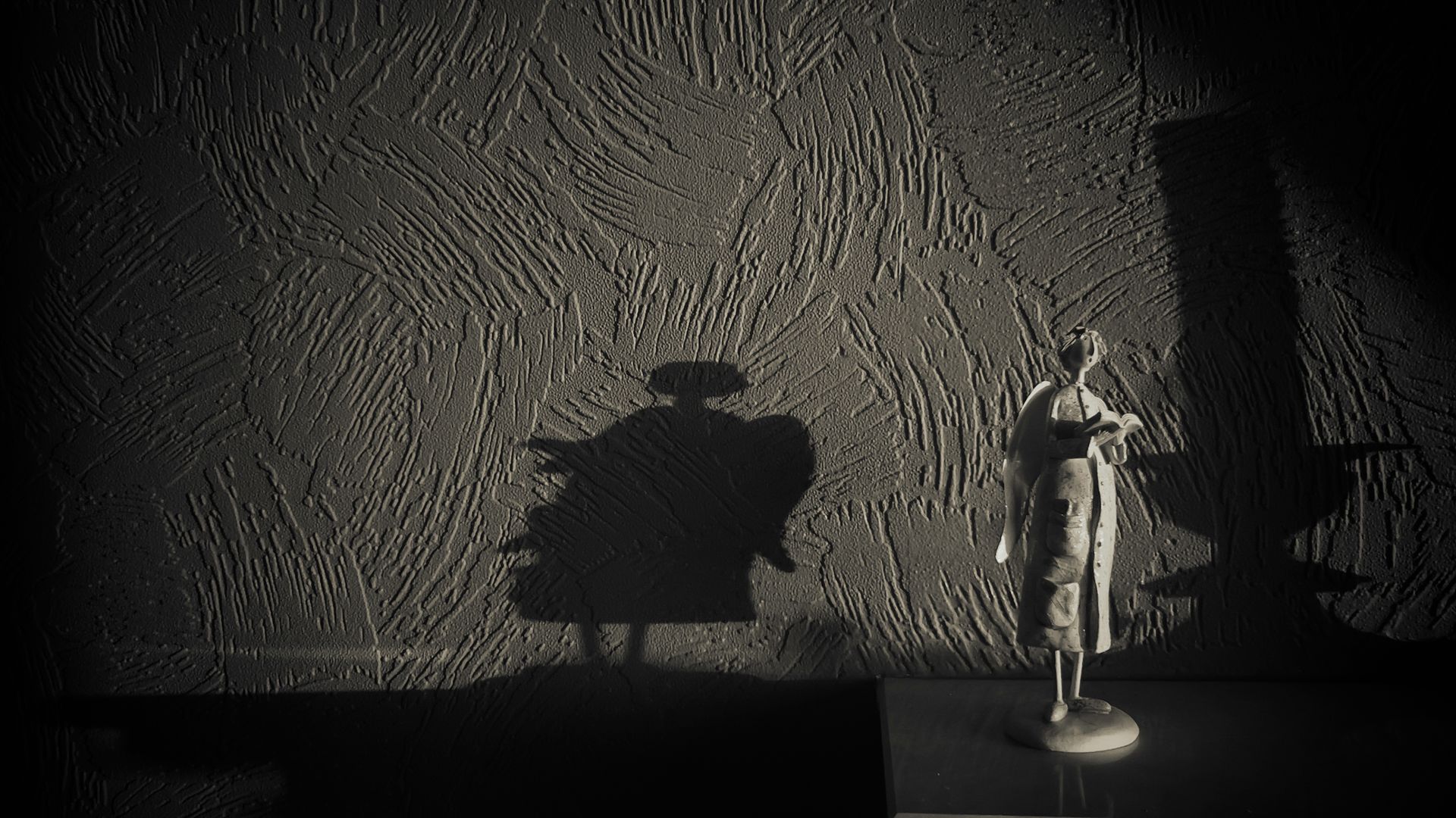 Small figurine standing against a textured wall, casting a large shadow in soft, dramatic light