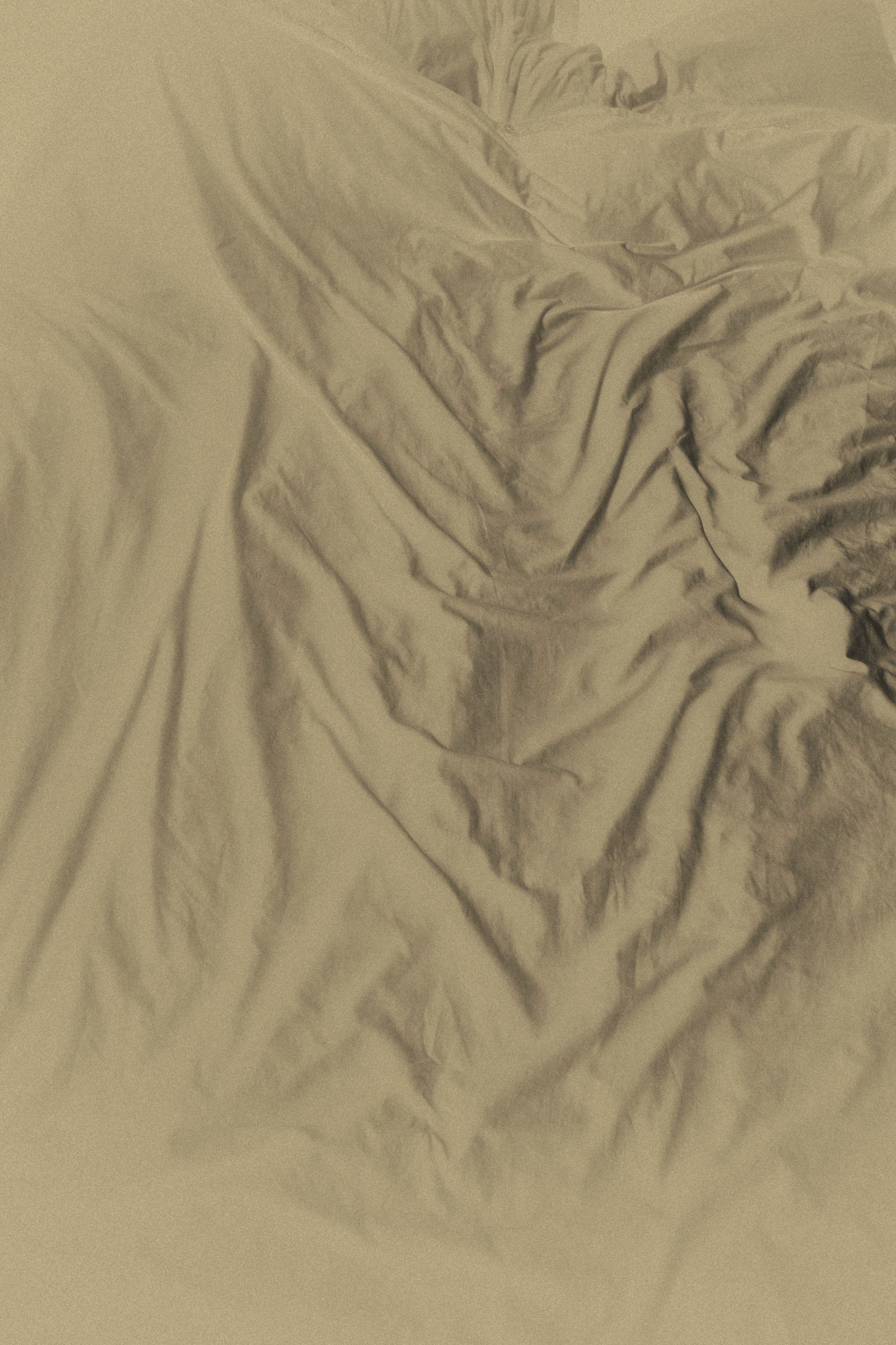 A faint imprint of a body on a crumpled bedsheet, left after waking — a trace of presence, fragile and ephemeral.