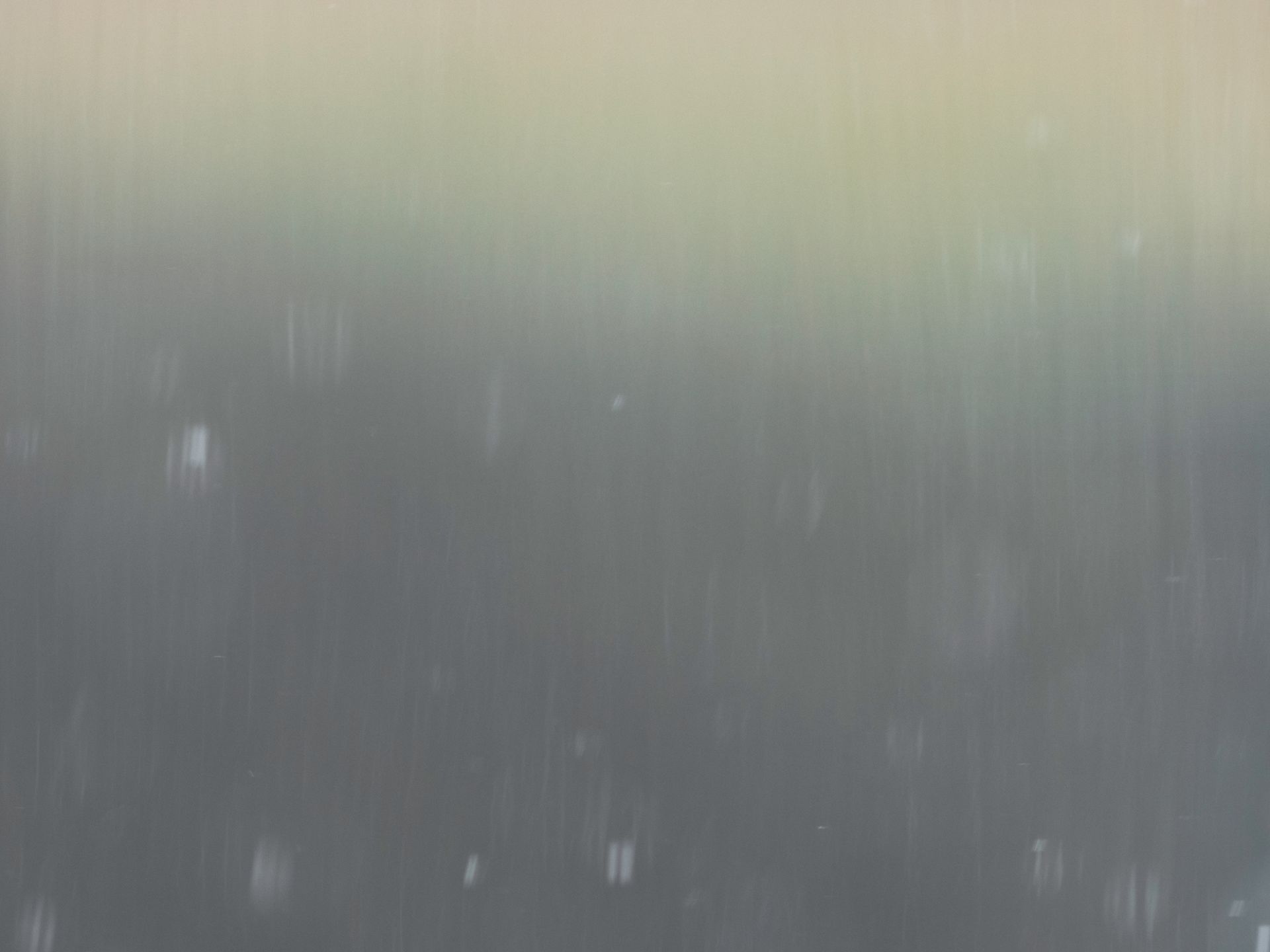 Raindrops on a window with blurred green and brown background.