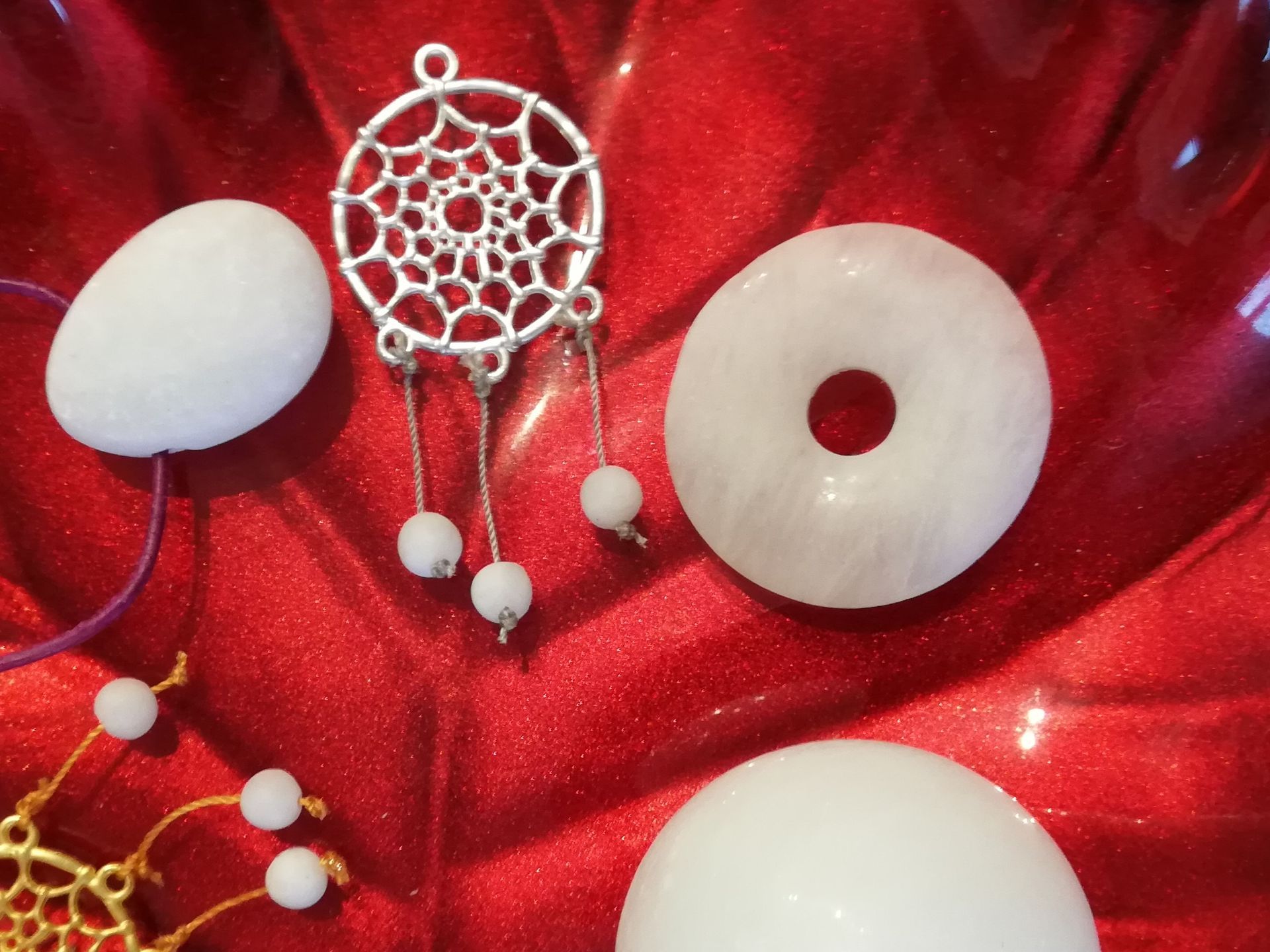 weißer Baryt auf rotem Grund. Gebohrter Trommelstein in Tropenform, Traumfänger und Donuts.